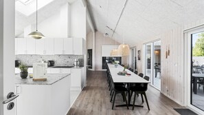 Eine moderne Küche mit weißen Schränken, einer Marmorarbeitsplatte und einem Essbereich mit einem langen Tisch und Stühlen.