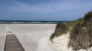 Ein sandiger Strand mit einer Holzpromenade, die zum Meer führt.