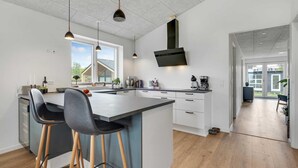 A modern kitchen with a central island, bar stools, a built-in oven, and a large window. - VillaVilla 950 - Spodsbjerg, Fyn og øer (Rudkøbing)