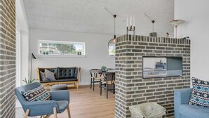 A modern living space with a brick fireplace, a sofa, a dining table, and a TV mounted on the wall. - VillaVilla 950 - Spodsbjerg, Fyn og øer (Rudkøbing)