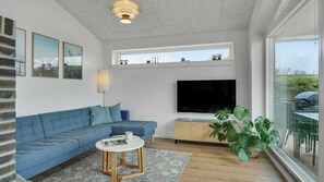 Ett modernt vardagsrum med en hörnsoffa, en platt-TV, ett runt soffbord och ett stort fönster med utsikt.