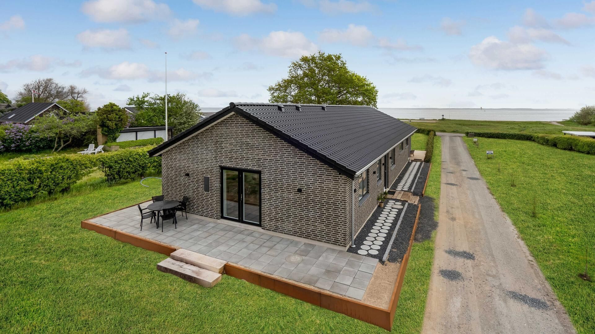 A modern house with a brick exterior, a patio with outdoor furniture, and a view of the sea.