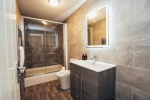 Ein modernes Badezimmer mit einer in Glas abgeschirmten Dusche, einem weißen Waschbecken und einem dunklen Holz-Waschtisch.