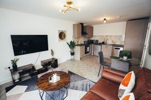 Ein modernes Wohnzimmer mit Fernseher, Sofa, Couchtisch und einer Küche im Hintergrund.
