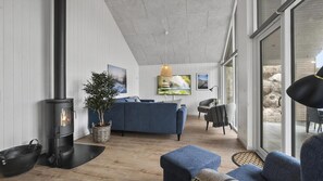 A modern living room with a fireplace, a sofa, a TV, and a view through large windows. - VillaVilla 928 - Hvide Sande, Vestjylland (Hvide Sande)