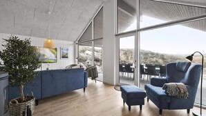 Un interior moderno con un amplio ventanal, un sofá azul, una zona de comedor y una planta.