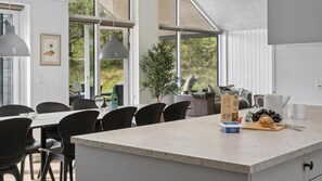 A modern kitchen with a large island, dining area with chairs, and a view of greenery outside. - VillaVilla 915 - Skåstrup Strand, Fyn og øer (Bogense)