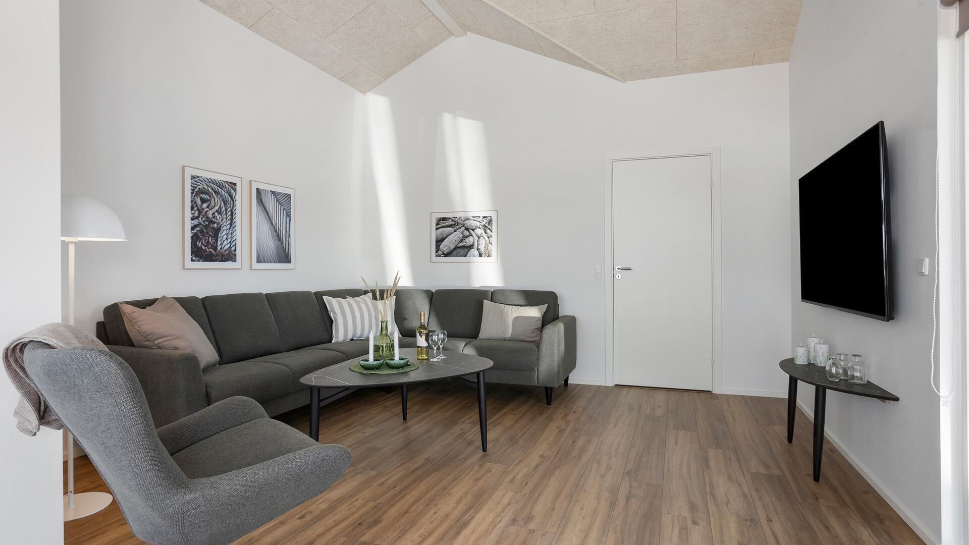 Uma sala de estar moderna com um sofá cinza, uma poltrona cinza, uma mesa de centro e uma TV de tela plana na parede.