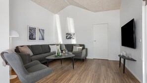 Ein modernes Wohnzimmer mit einem grauen Sofa, einem grauen Sessel, einem Couchtisch und einem an der Wand befestigten Flachbildfernseher.