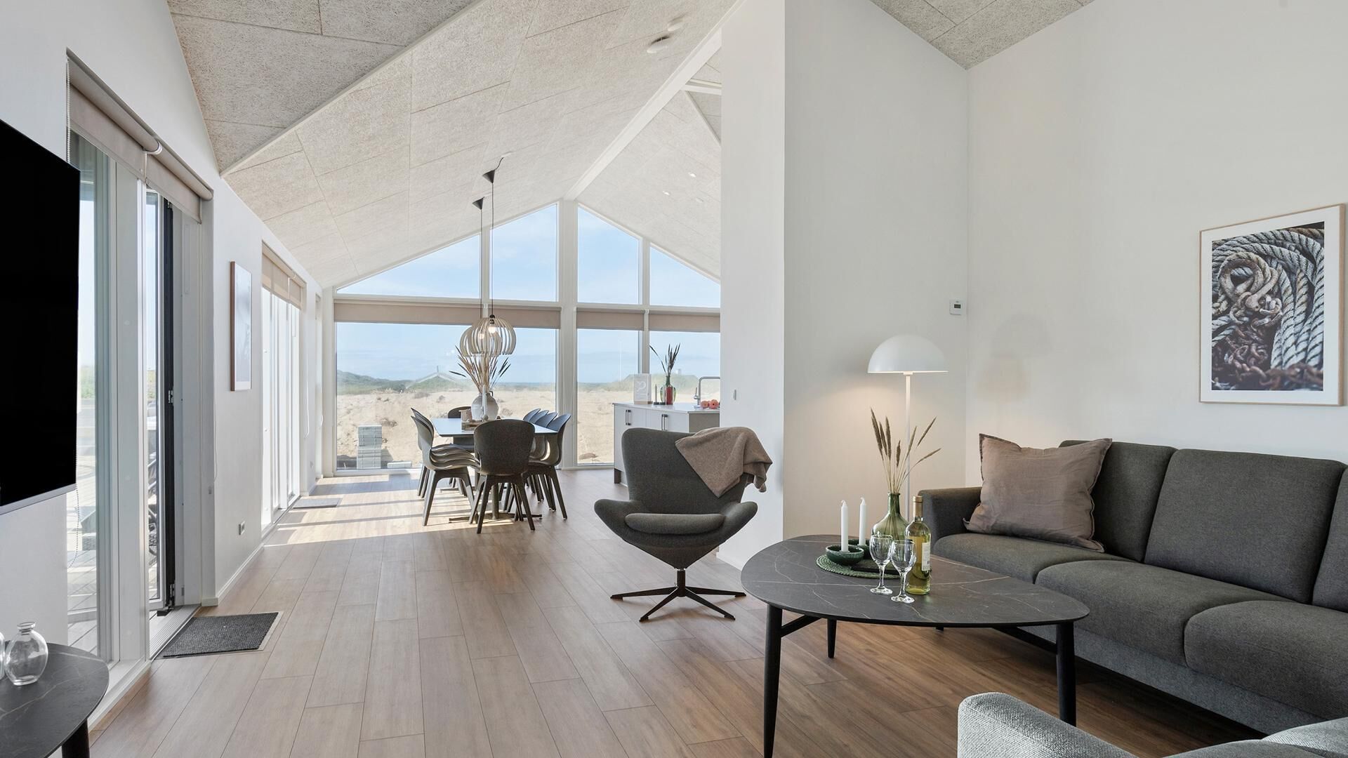 Uma sala de estar ampla, com teto alto, mesa de jantar com cadeiras, sofá e mesa de centro com objetos decorativos.