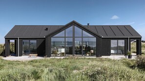 Ein modernes Haus mit großen Glasfenstern, einem geneigten Dach und Blick auf die umliegende Landschaft.