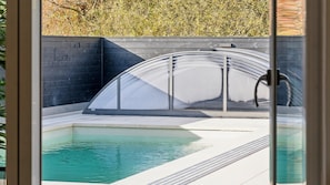 Ein Swimmingpool mit Glasveranda, einer Backsteinmauer und blauem Himmel.