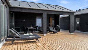 Ein überdachter Außenbereich mit einer Holzterrasse, einem Tisch mit Stühlen und einem Liegestuhl.