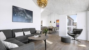 Uma sala moderna com um sofá cinzento, uma mesa de centro redonda e um espaço de jantar com cadeiras.