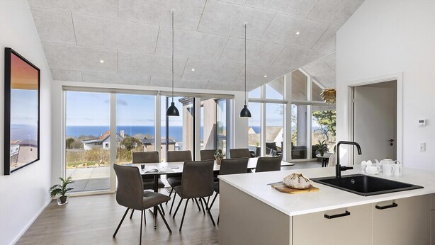 Cozinha moderna com uma ilha grande, área de jantar com cadeiras e janelas amplas com vista para o mar.