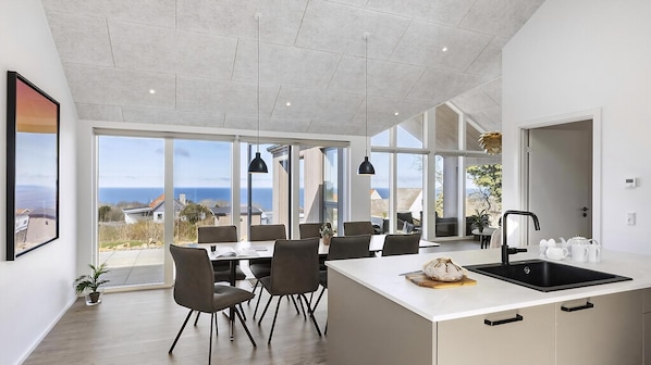 A modern kitchen with a large island, dining area with chairs, and large windows offering a view of the sea. - VillaVilla 927 - Hasle, Bornholm (Hasle)