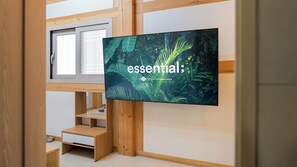 Una habitación moderna con una gran televisión de pantalla plana montada en la pared, estanterías de madera, una ventana y una pequeña mesa de madera.