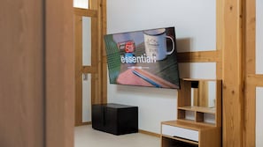 A modern room with a wooden wall structure, a television mounted on the wall, a black storage box, and a wooden shelf unit.