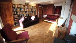 A living room with a herringbone floor, a sofa, a chair, a bookshelf, and a guitar. - Rustic cottage with sea views (Southwick)
