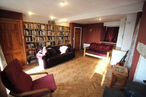 Ein Wohnzimmer mit Fischgrätparkett, einer Couch, einem Sessel, einem Bücherregal und einer Gitarre.