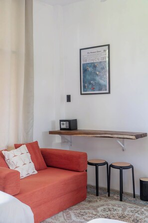 A room with a red sofa, two stools, a framed picture on the wall, and a small shelf with a radio.