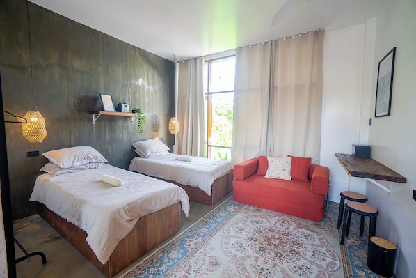 A bedroom with two beds, a red sofa, a patterned rug, and a window with curtains.