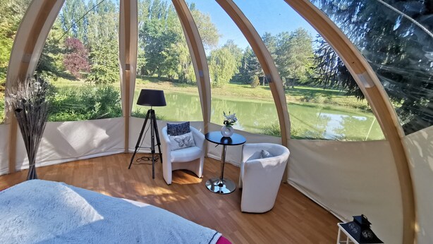 Una habitación con forma de cúpula, que ofrece vistas a un campo de golf, una lámpara de trípode, una mesita y una silla blanca.