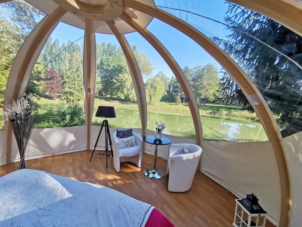 Une pièce en forme de dôme offrant une vue sur un terrain de golf, avec un lampadaire sur trépied, une petite table et une chaise blanche.