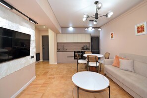 Eine moderne Küche mit weißen Schränken, ein Essbereich mit rundem Tisch und Stühlen sowie ein Wohnbereich mit einer Couch und Kissen.