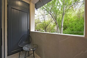 Een balkon met uitzicht op bomen, een deur en een stoel.