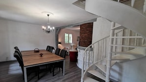 A dining area with a wooden table and chairs, a chandelier, a staircase, and a stone wall. - Bed and Breakfast 'Chambre D'hôte Vue Sur Étang' with Shared Pool, Shared Terrace and Wi-Fi (Chitenay)
