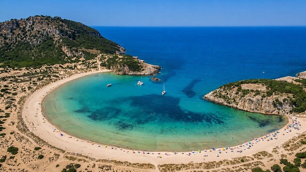 Vista aèria d'una platja costanera amb aigües turqueses cristal·lines, un litoral sorrenc i roques.