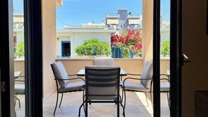 Una porta corredissa oberta que dona a un balcó amb taula i cadires, vista a edificis i un cel serè.