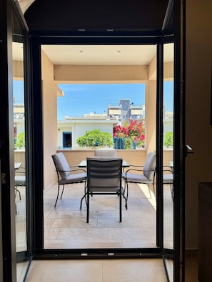 Eine offene Schiebetür führt zu einem Balkon mit Tisch und Stühlen, Blick auf Gebäude und klarem Himmel.