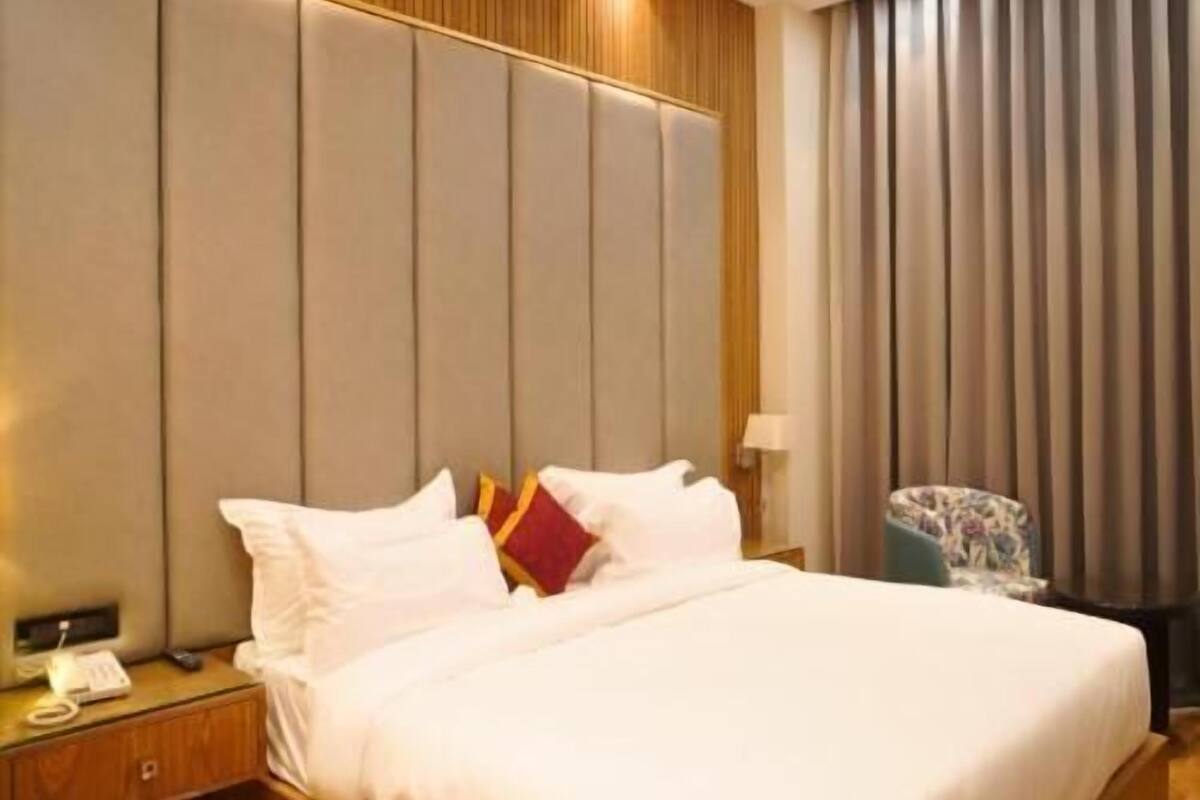 A hotel room with a large bed, a wooden headboard, a nightstand with a phone, and a chair.
