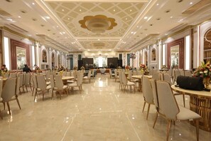 Un amplio salón de banquetes con techos altos, candelabros y filas de mesas y sillas.
