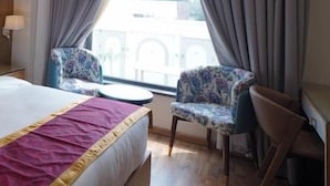 Una habitación de hotel con cama, dos sillas, una mesa redonda y un ventanal con cortinas.