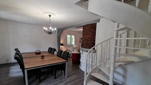 A dining area with a wooden table and chairs, a chandelier, a staircase, and a stone wall. - Bed and Breakfast 'Chambre Quadruple' with Shared Pool, Shared Terrace and Wi-Fi (Chitenay)