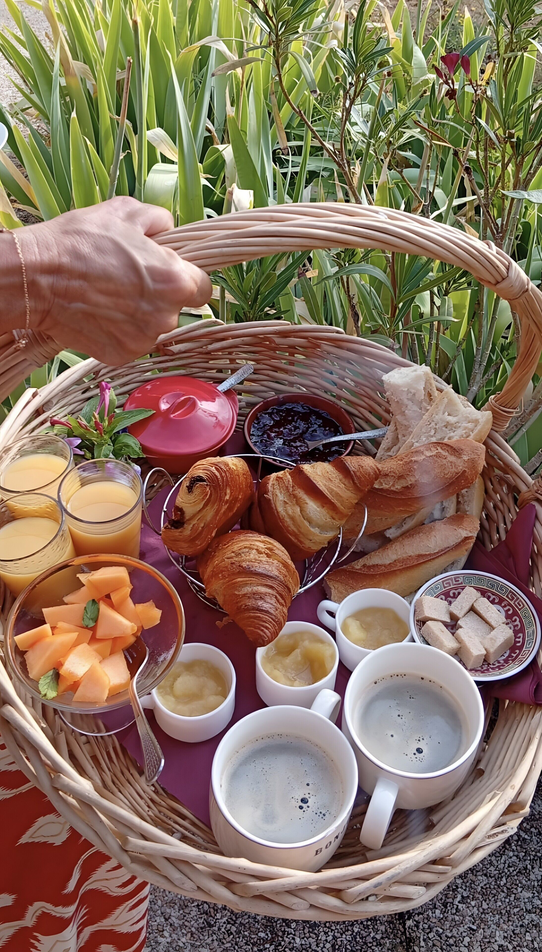 Un panier en osier rempli de nourriture et de boissons, notamment des croissants, du pain et diverses boissons.