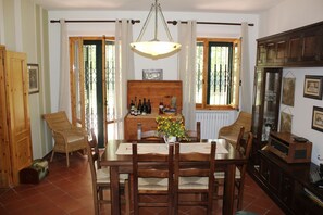 A dining area with a wooden table, chairs, a chandelier, and a window with curtains. - Villa Smirra by MMega (Smirra)