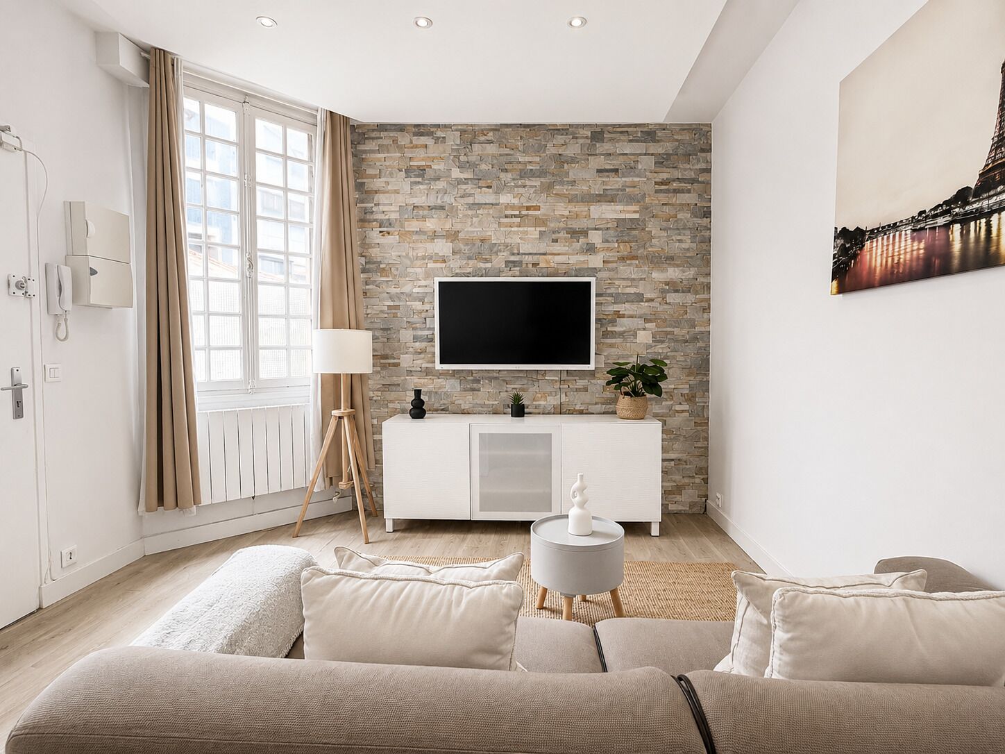 A modern living room with a stone wall, a flat-screen TV, a white cabinet, and a beige sofa.
