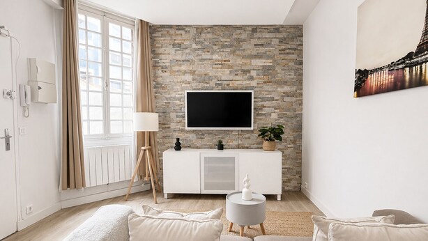 A modern living room with a stone wall, a flat-screen TV, a white cabinet, and a beige sofa. - Luxueux Appartement au 16e  (Paris)