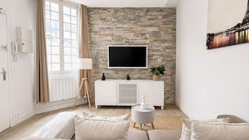A modern living room with a stone wall, a flat-screen TV, a white cabinet, and a beige sofa.