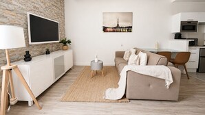 A modern living room with a flat-screen TV, a sofa, a dining area, and a kitchen. - Luxueux Appartement au 16e  (Paris)