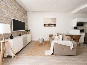 Ein modernes Wohnzimmer mit Flachbildfernseher, einer Couch, einer Essecke und einer Küche.