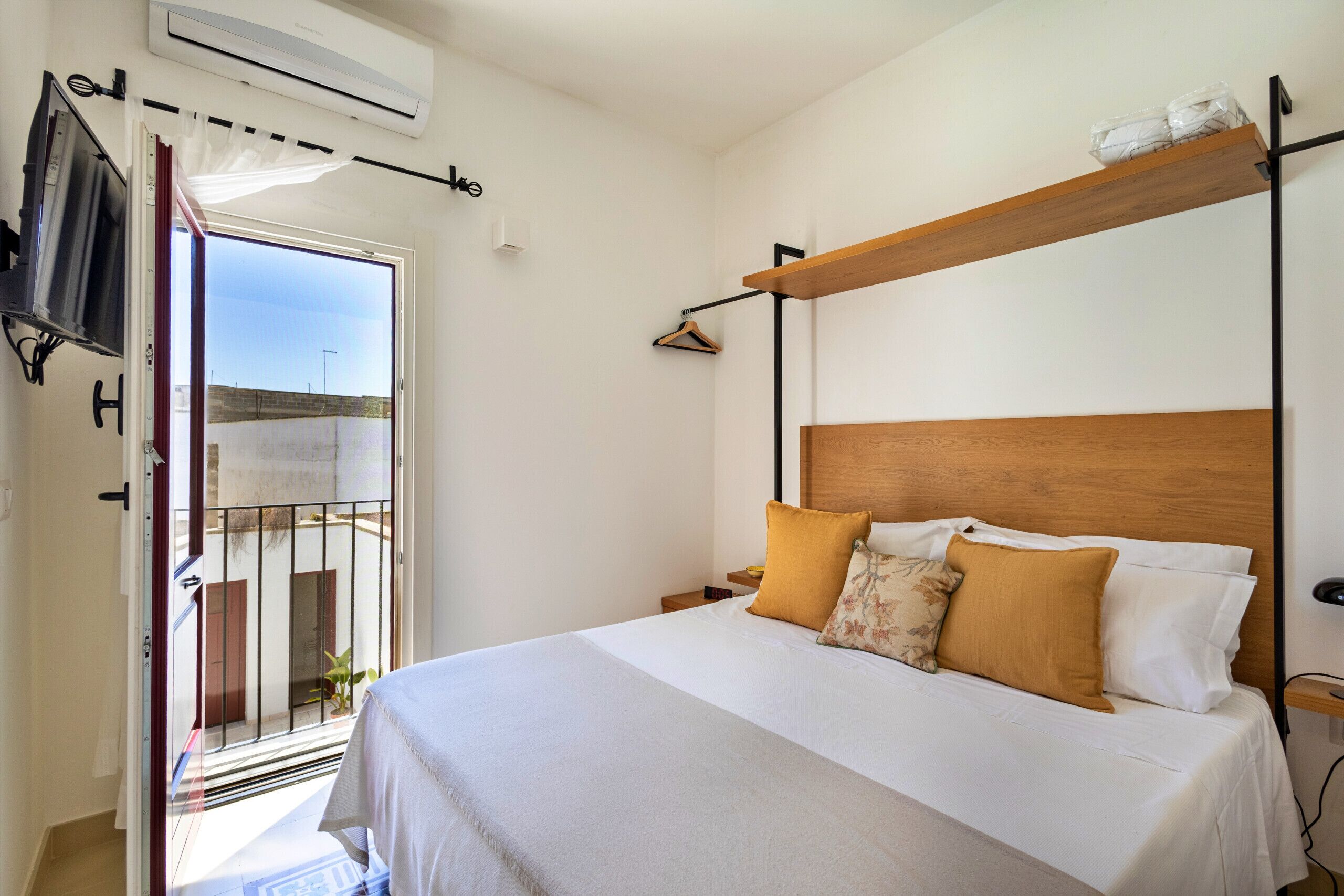A bedroom with a bed, a TV, a wooden shelf, and a balcony.