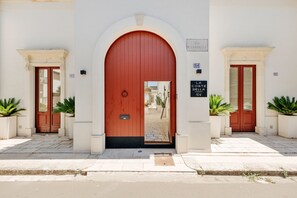 A building with a red arched entrance, numbered doors, and potted plants. - La Corte Bella (Leverano)