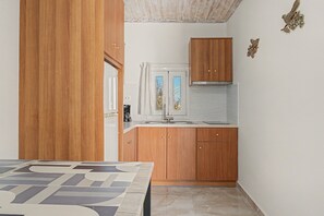 Cocina compacta con armarios de madera, un lavamanos de acero inoxidable y un ventanal con cortinas.