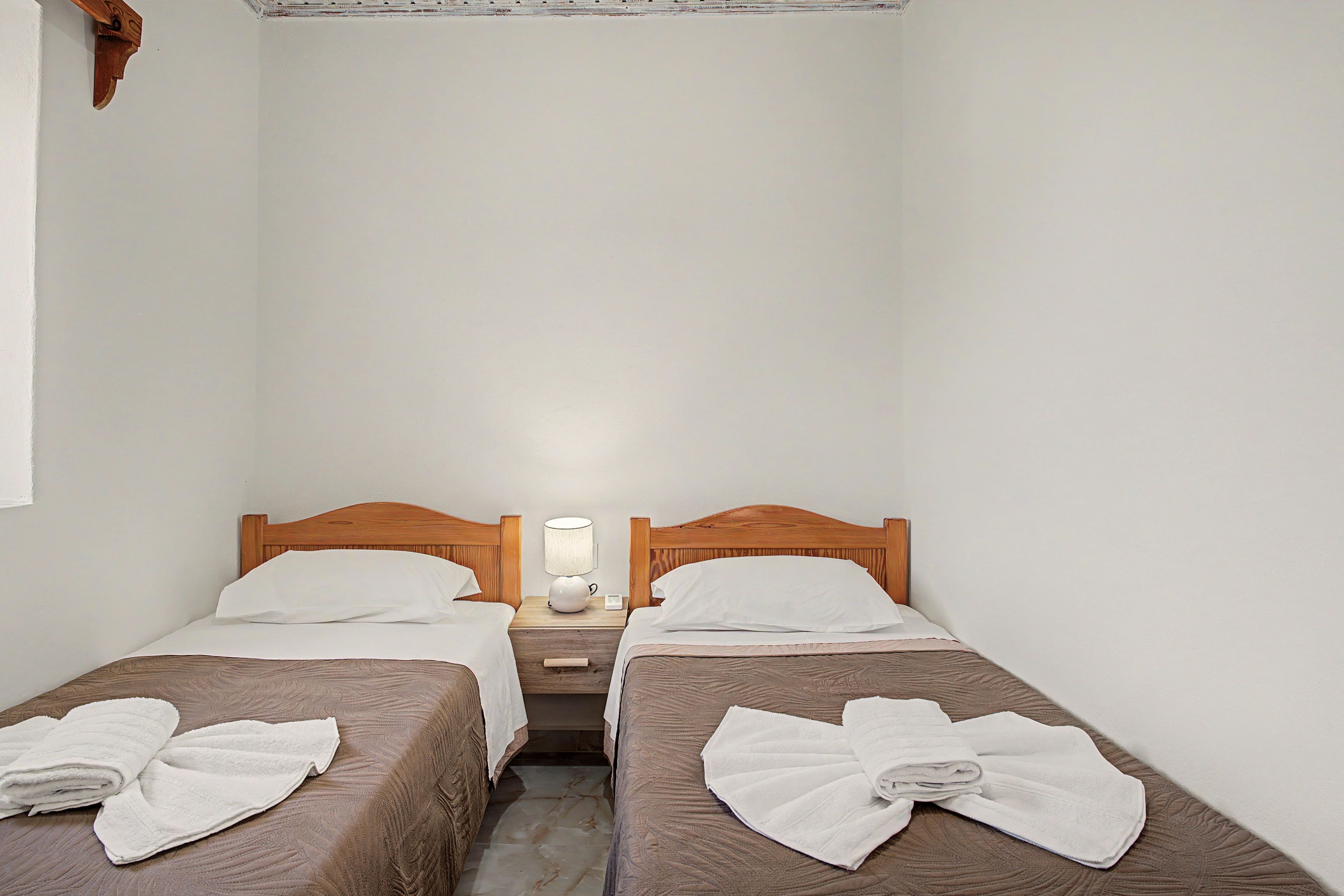 A small hotel room with two single beds, a nightstand with a lamp, and a wooden headboard.