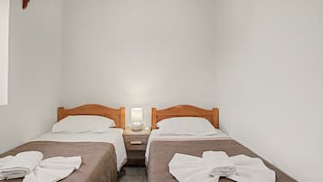 A small hotel room with two single beds, a nightstand with a lamp, and a wooden headboard.